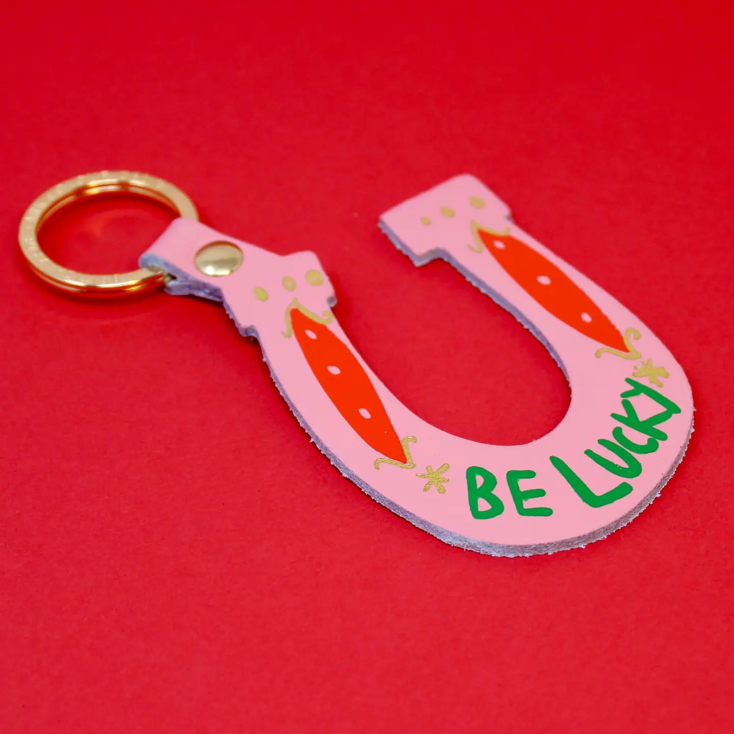 Pink horseshoe keychain with 'Be Lucky' text on a red background