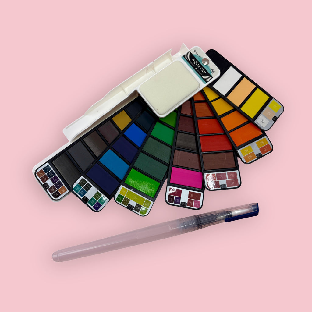 Fan-style watercolor palette with water brush, shown open against a pink background.