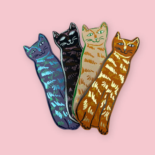 Four leather cat-shaped bookmarks in blue, black, cream, and orange on a pale pink background.