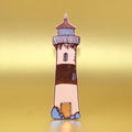 Peach lighthouse-shaped leather bookmark from an Ark Colour Design book, shown standing on a gold background.