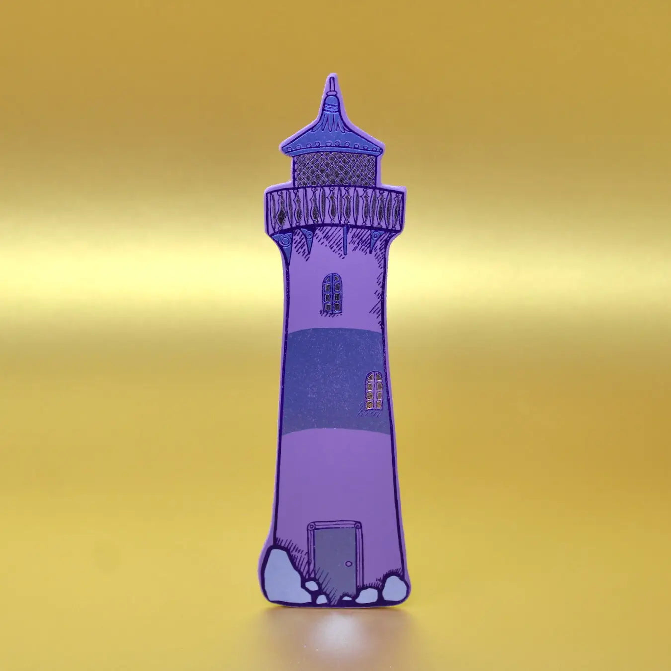 Lilac lighthouse-shaped leather bookmark from an Ark Colour Design book, shown standing on a gold background.