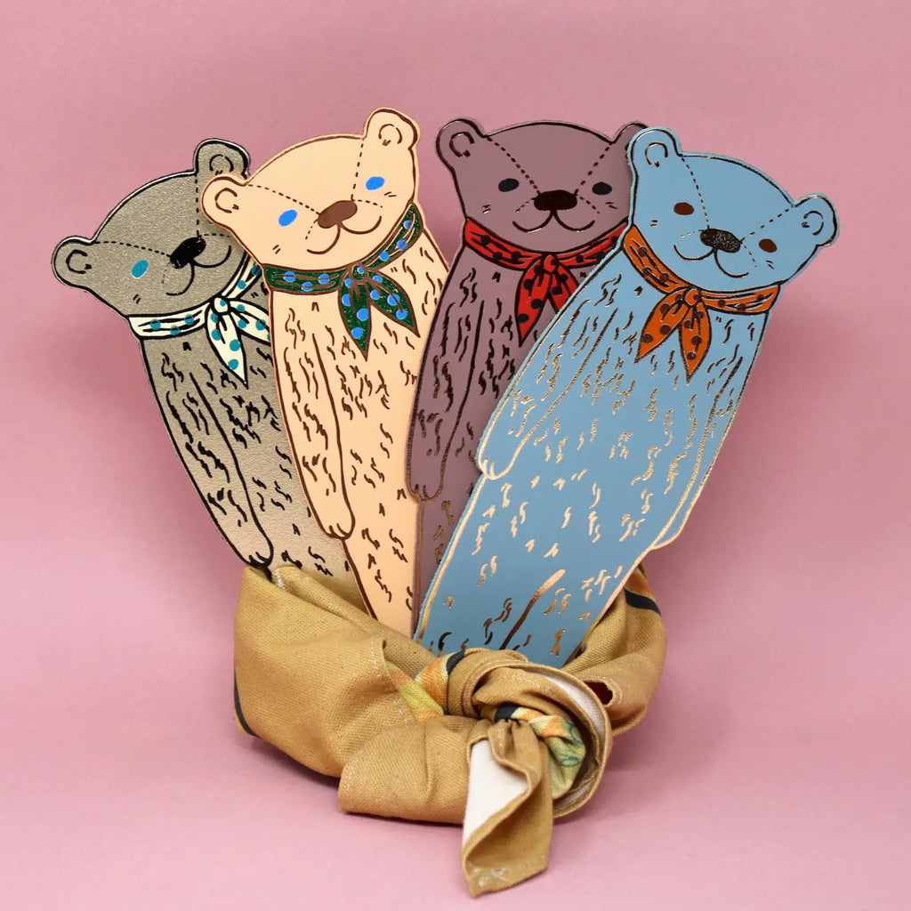 Set of colorful Ark Colour Design leather bookmarks shaped like bears, arranged in a fabric bundle on a pink background.