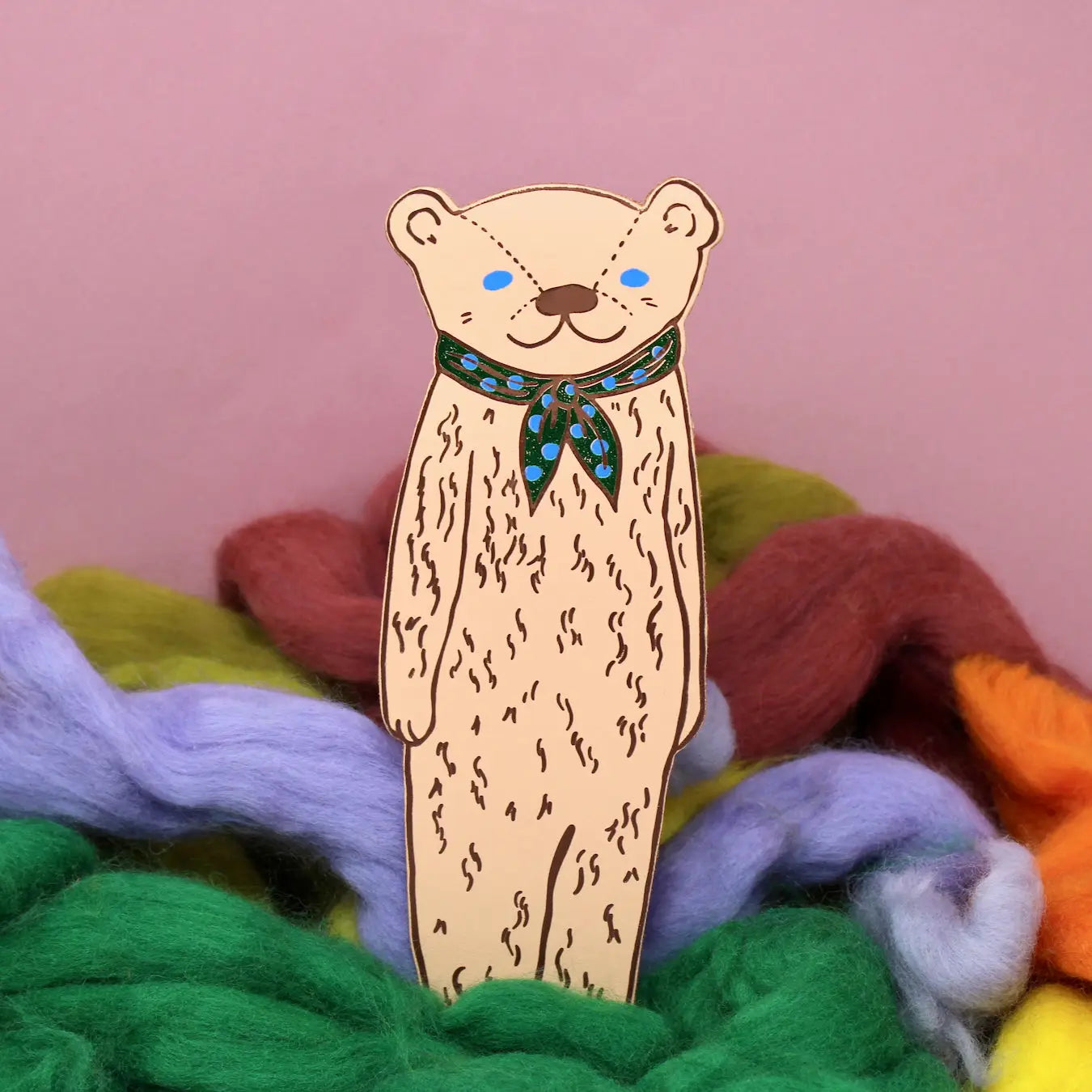 Ark Colour Design leather bookmark in cream shaped like a bear wearing a red scarf, shown standing among colorful wool on a pink background