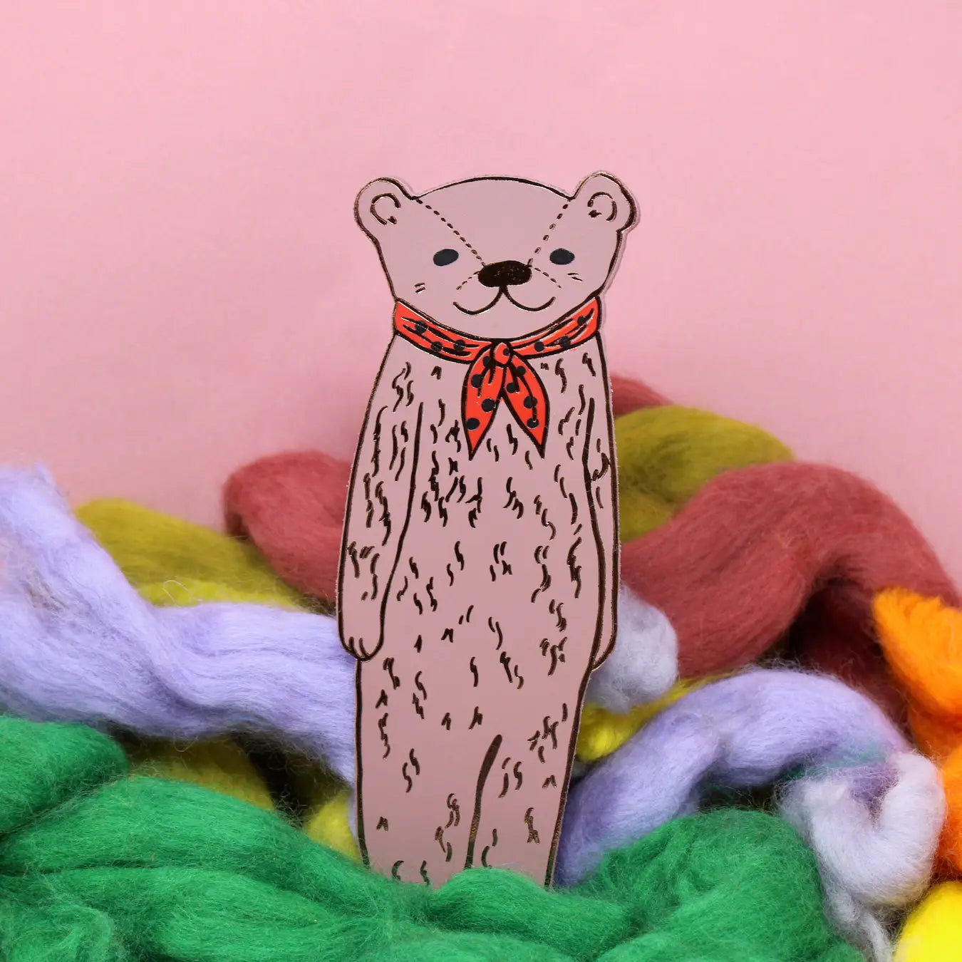 Ark Colour Design leather bookmark in dusty pink shaped like a bear wearing a red scarf, shown standing among colorful wool on a pink background.