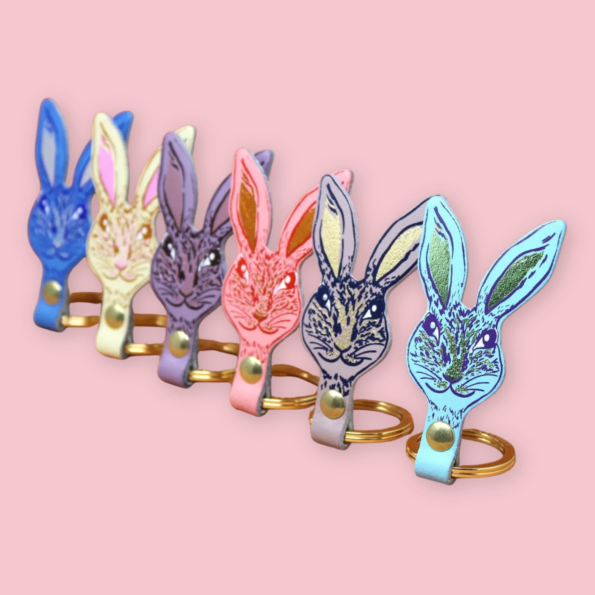 Ark Colour Design rabbit keychains in assorted colors, arranged in a row with gold rings on a pink background.