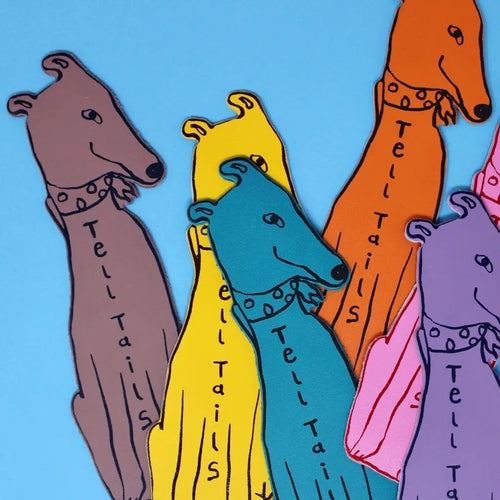 Greyhound-shaped bookmarks in brown, yellow, teal, orange, pink, and purple, each lettered "Tell Tails" with a spotted collar, fanned out on a blue background.