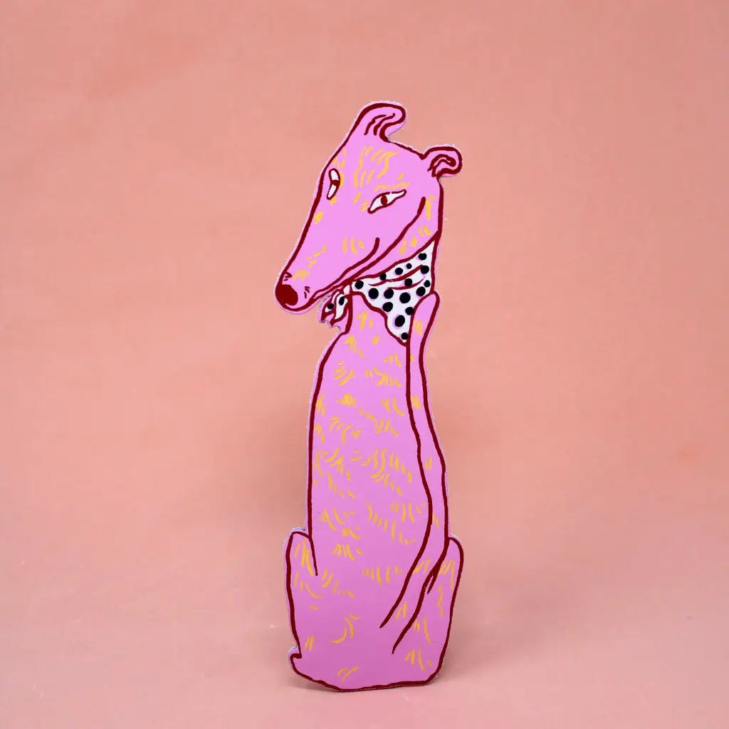 Pink greyhound-shaped bookmark wearing a black polka dot bandana, sitting upright, on a peach background.