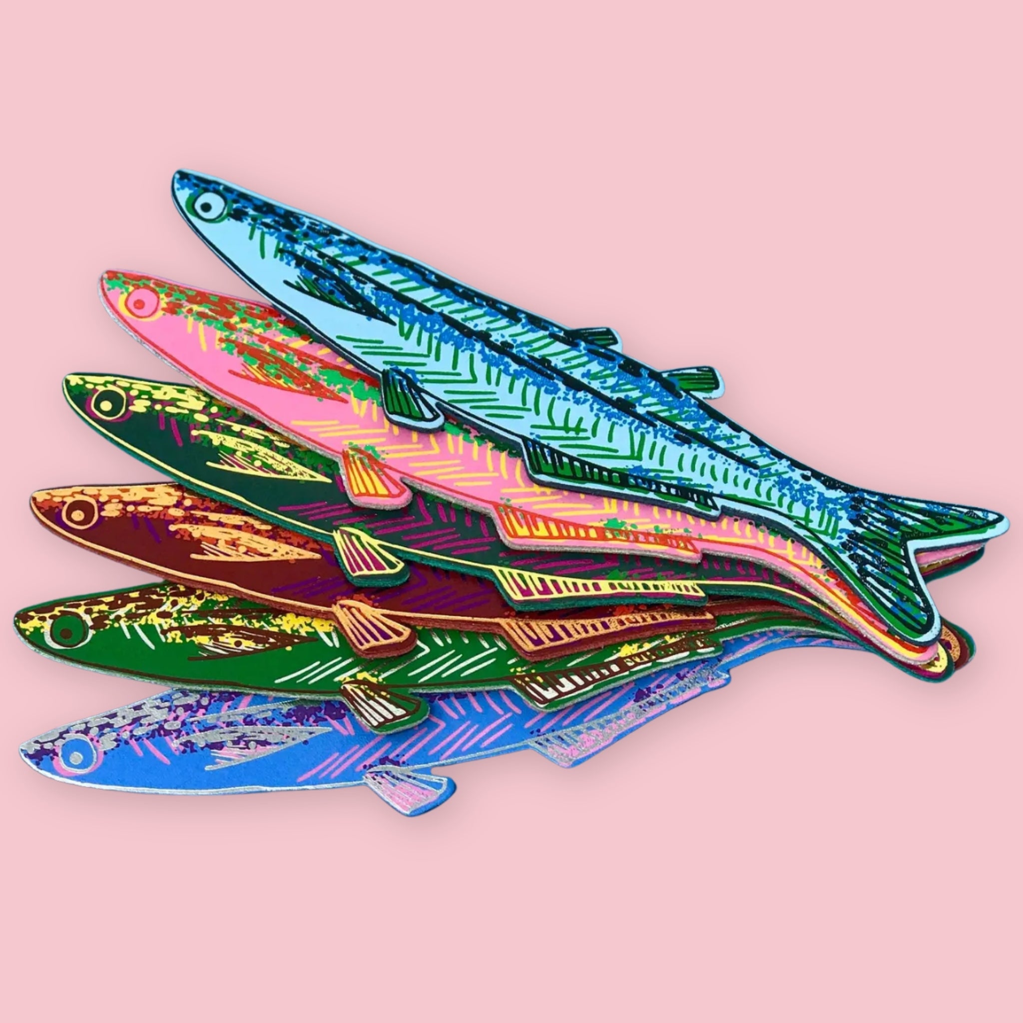Six fish-shaped bookmarks in light blue, pink, green, brown, dark green, and blue, each with patterned scales, fanned out on a pink background.