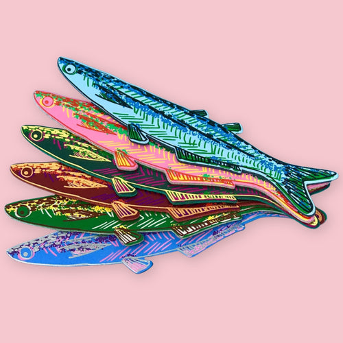 Six fish-shaped bookmarks in light blue, pink, green, brown, dark green, and blue, each with patterned scales, fanned out on a pink background.