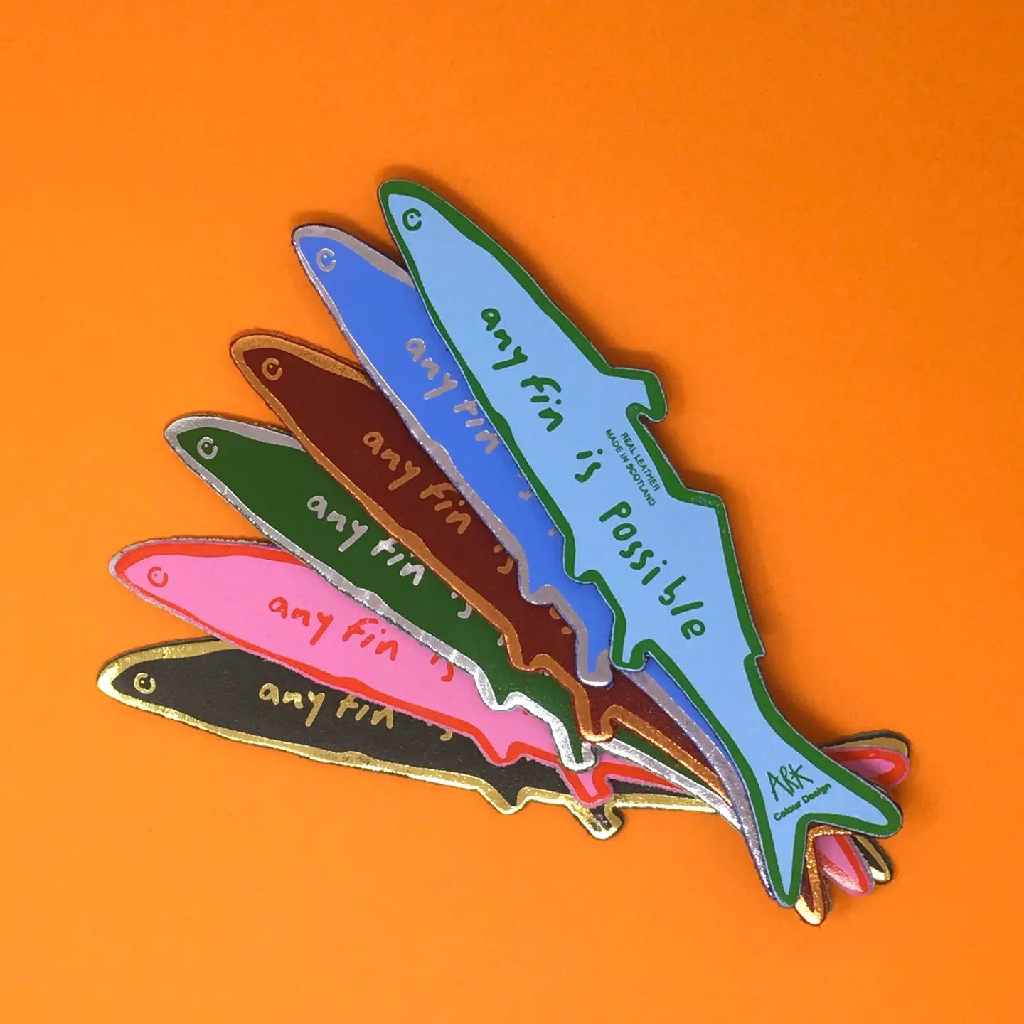 Six fish-shaped bookmarks in blue, green, brown, pink, dark green, and black, each lettered "Any fin is possible, Ark Colour Design," fanned out on an orange background.