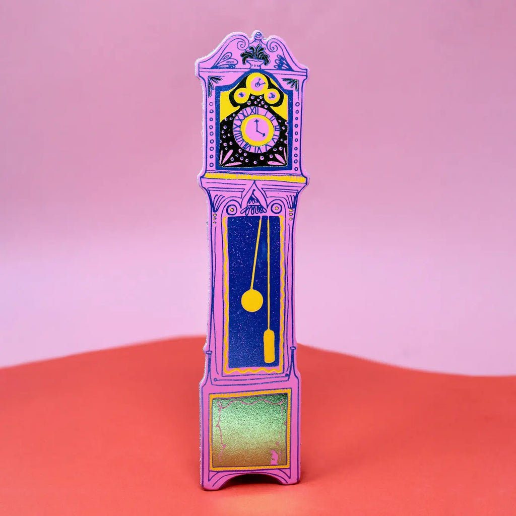 Hot pink Ark Colour Design leather bookmark shaped like a colorful grandfather clock, shown standing on a pink and red background.
