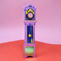 Hot pink Ark Colour Design leather bookmark shaped like a colorful grandfather clock, shown standing on a pink and red background.
