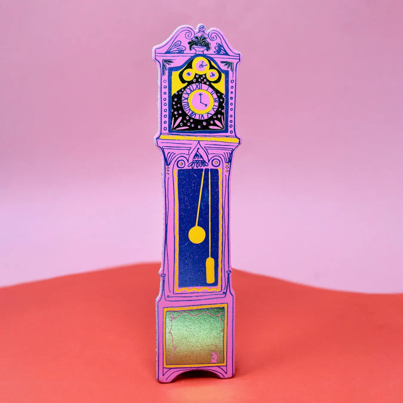 Hot pink Ark Colour Design leather bookmark shaped like a colorful grandfather clock, shown standing on a pink and red background.