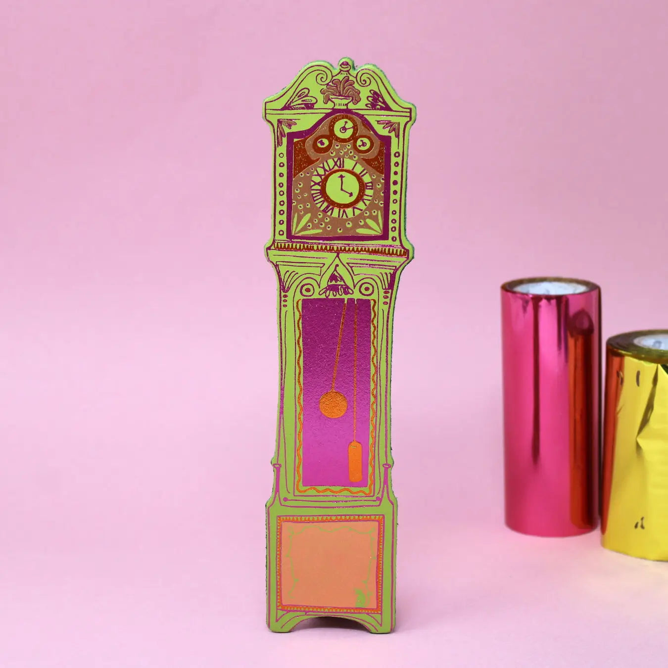 Apple green Ark Colour Design leather bookmark shaped like a colorful grandfather clock, shown standing on a pink background.