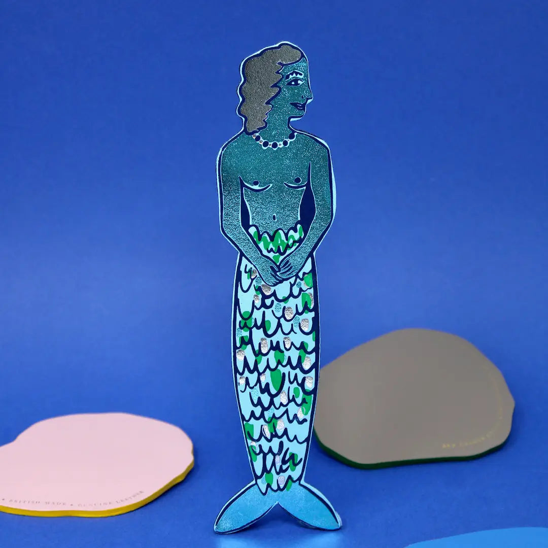 Ark Colour Design leather bookmark shaped like a mermaid, shown standing on a blue background.