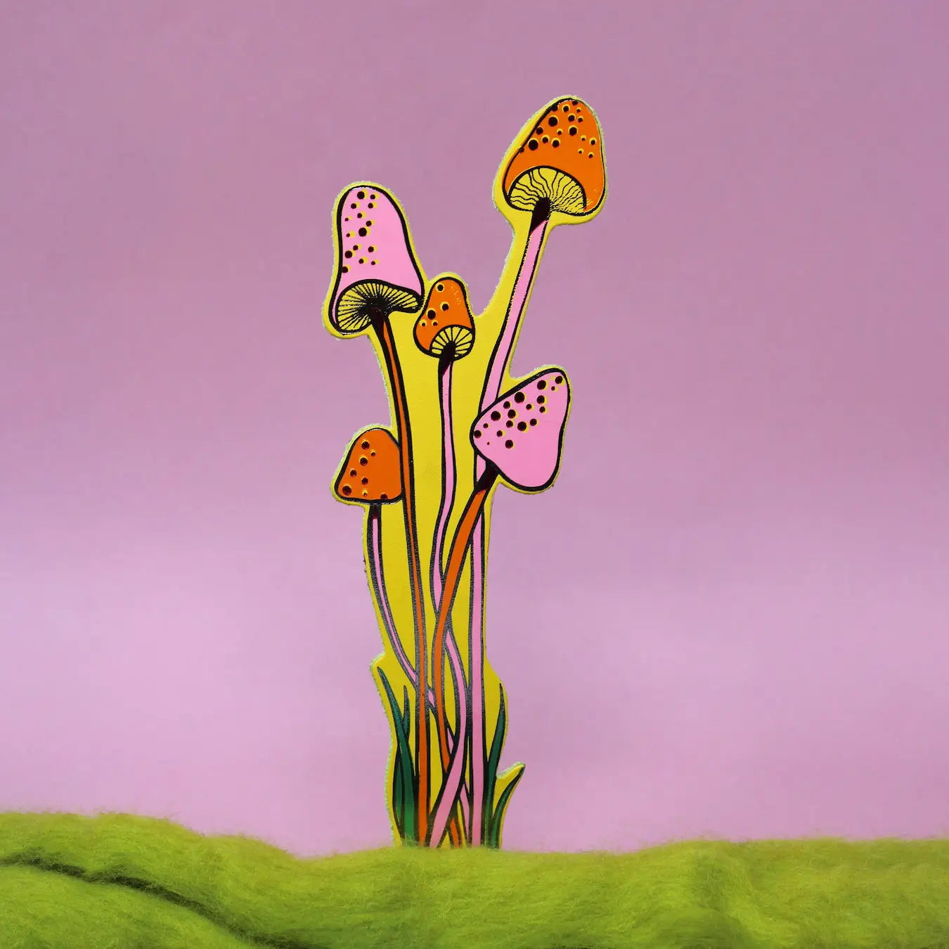 Pink, yellow and orange spotted mushroom-shaped bookmark rising from yellow moss, on a green background.