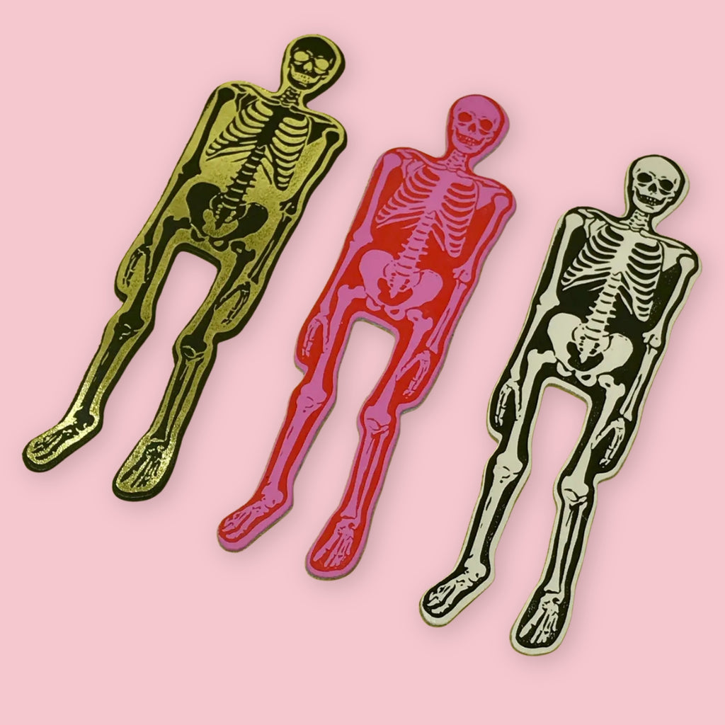 Ark Colour Design skeleton bookmarks in black, pink, and white colorways, arranged on a pink background.