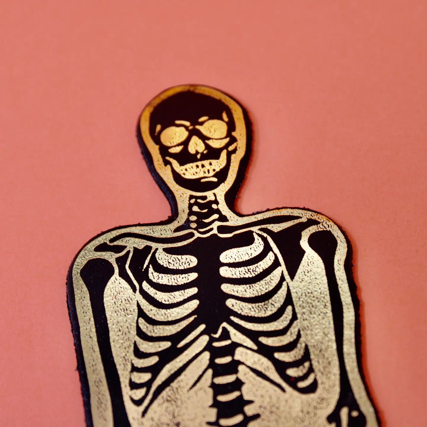 Ark Colour Design skeleton bookmark in black and gold, shown close up on an orange background.
