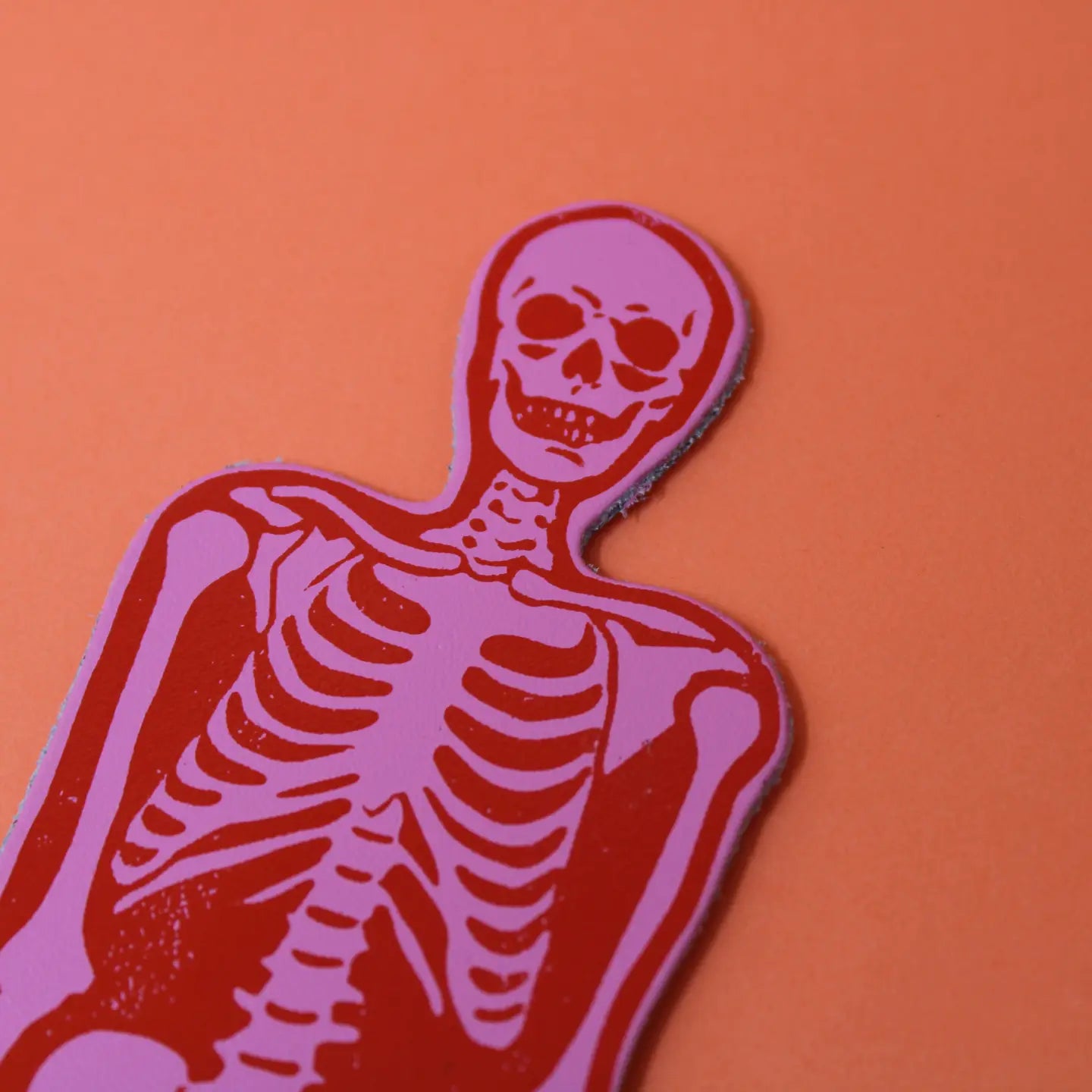 Ark Colour Design skeleton bookmark in pink and red, shown close up on an orange background.