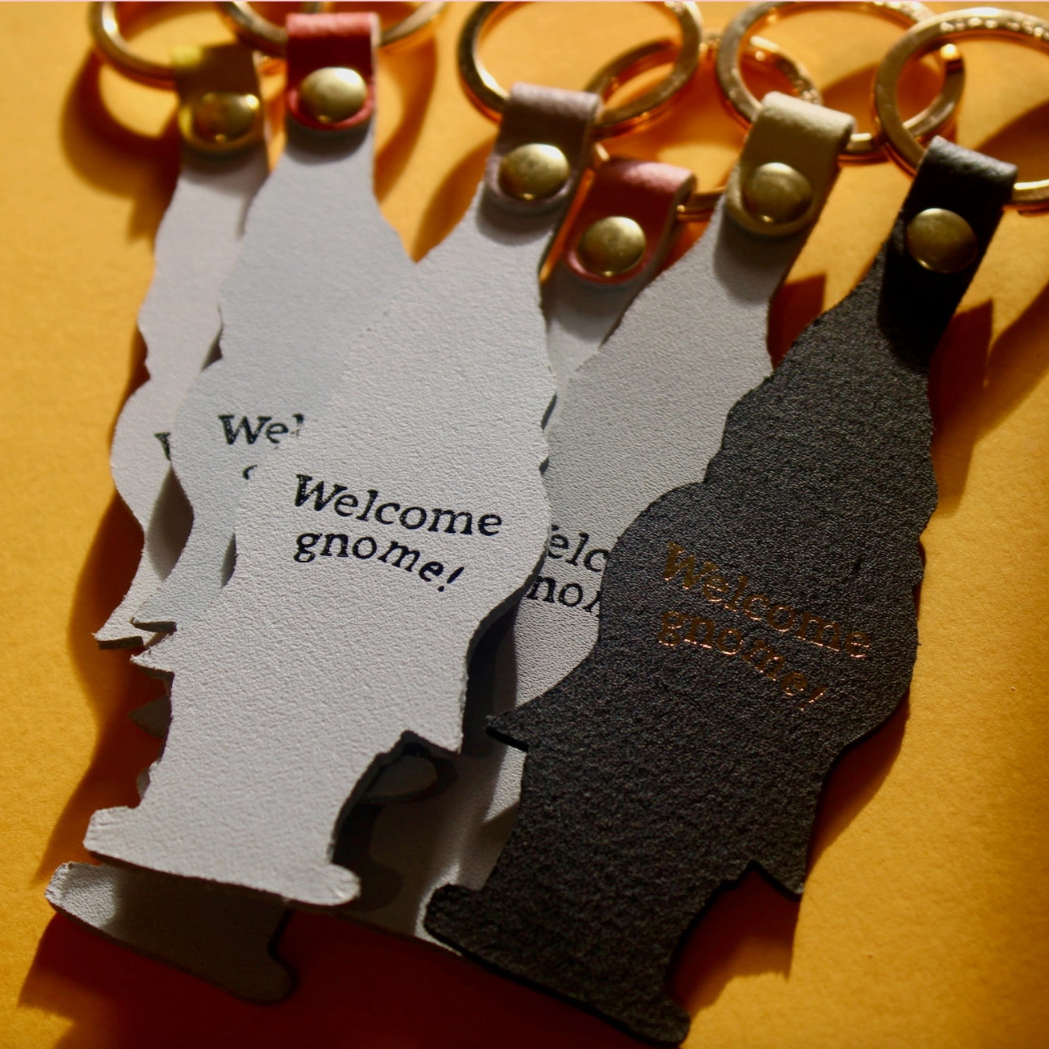 Back side of Ark Colour Design gnome keychains with gold rings and “Welcome gnome!” text.