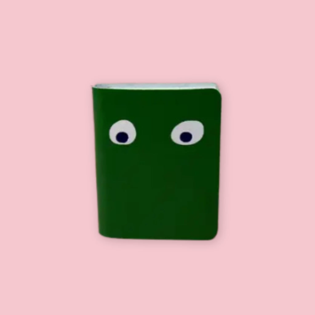 Ark Colour Design leather googly eye notebook in dark green with foil-embossed eyes on a pink background
