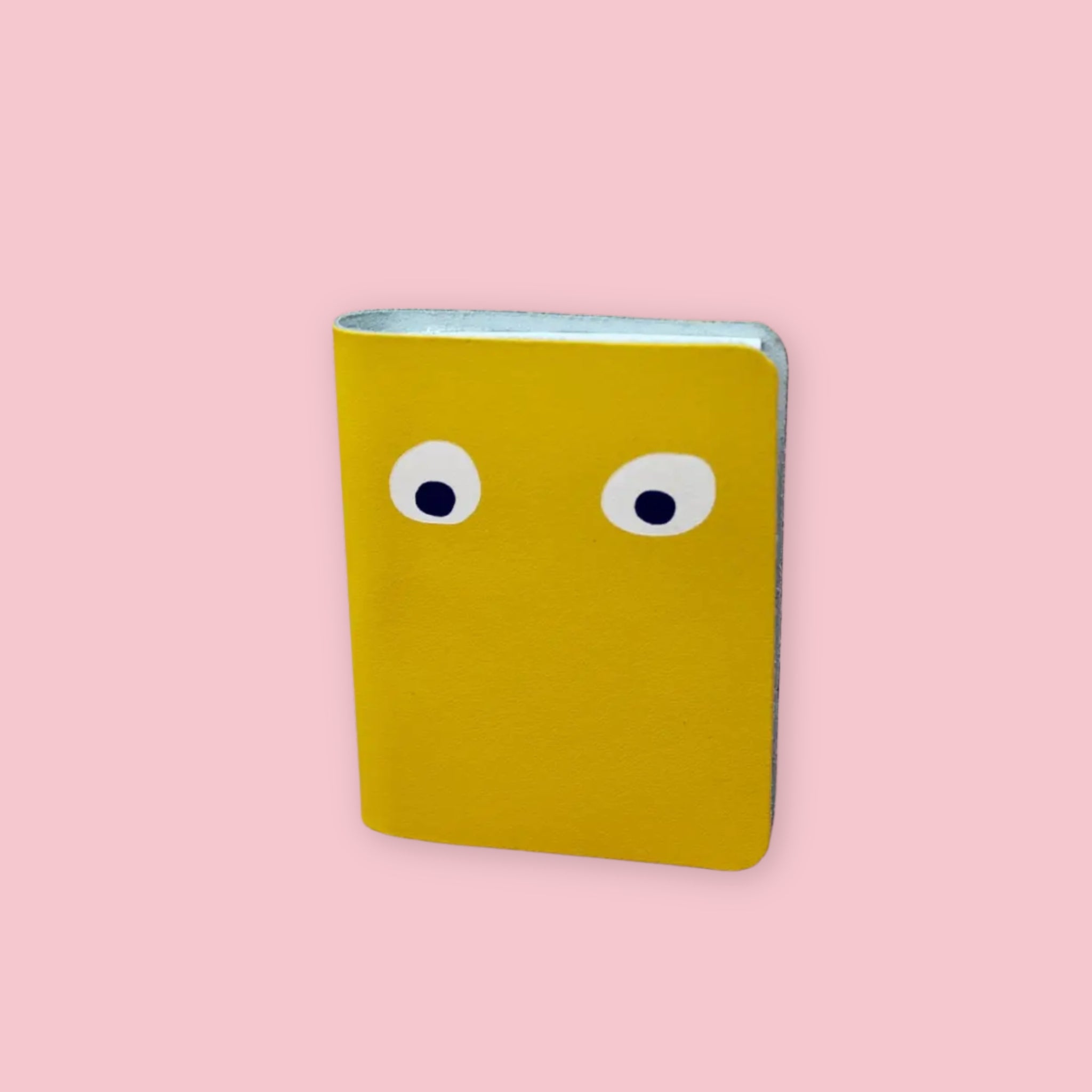 Ark Colour Design leather googly eye notebook in yellow with foil-embossed eyes on a pink background
