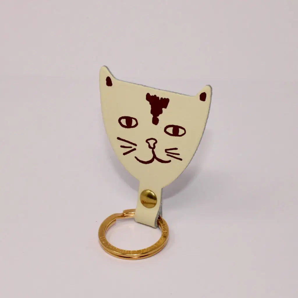 Ark Colour Design cream cat keychain with a gold ring and hand-drawn burgundy cat face design.