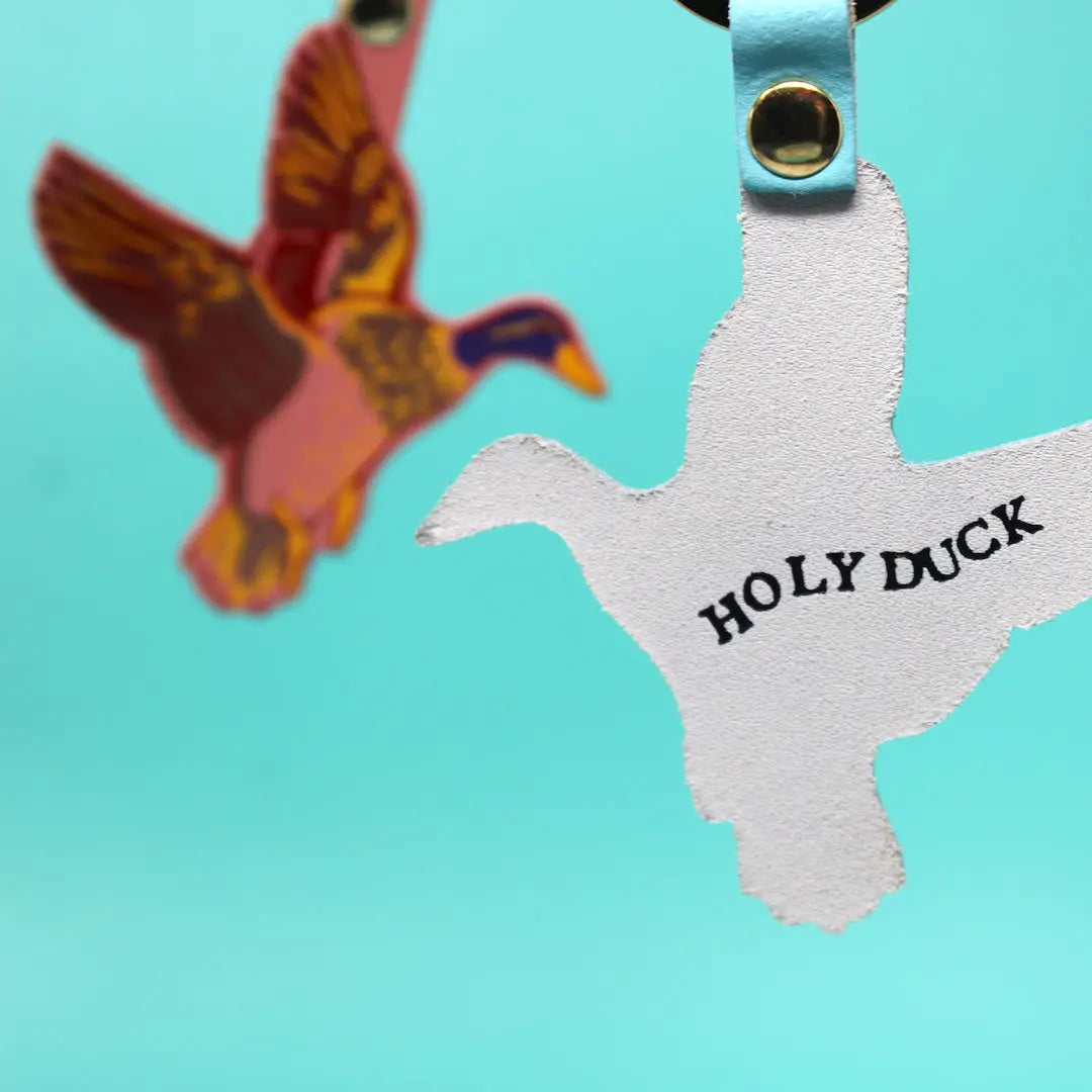 Back side of Ark Colour Design flying duck keychain with “Holy Duck” text, blue strap, and gold ring.