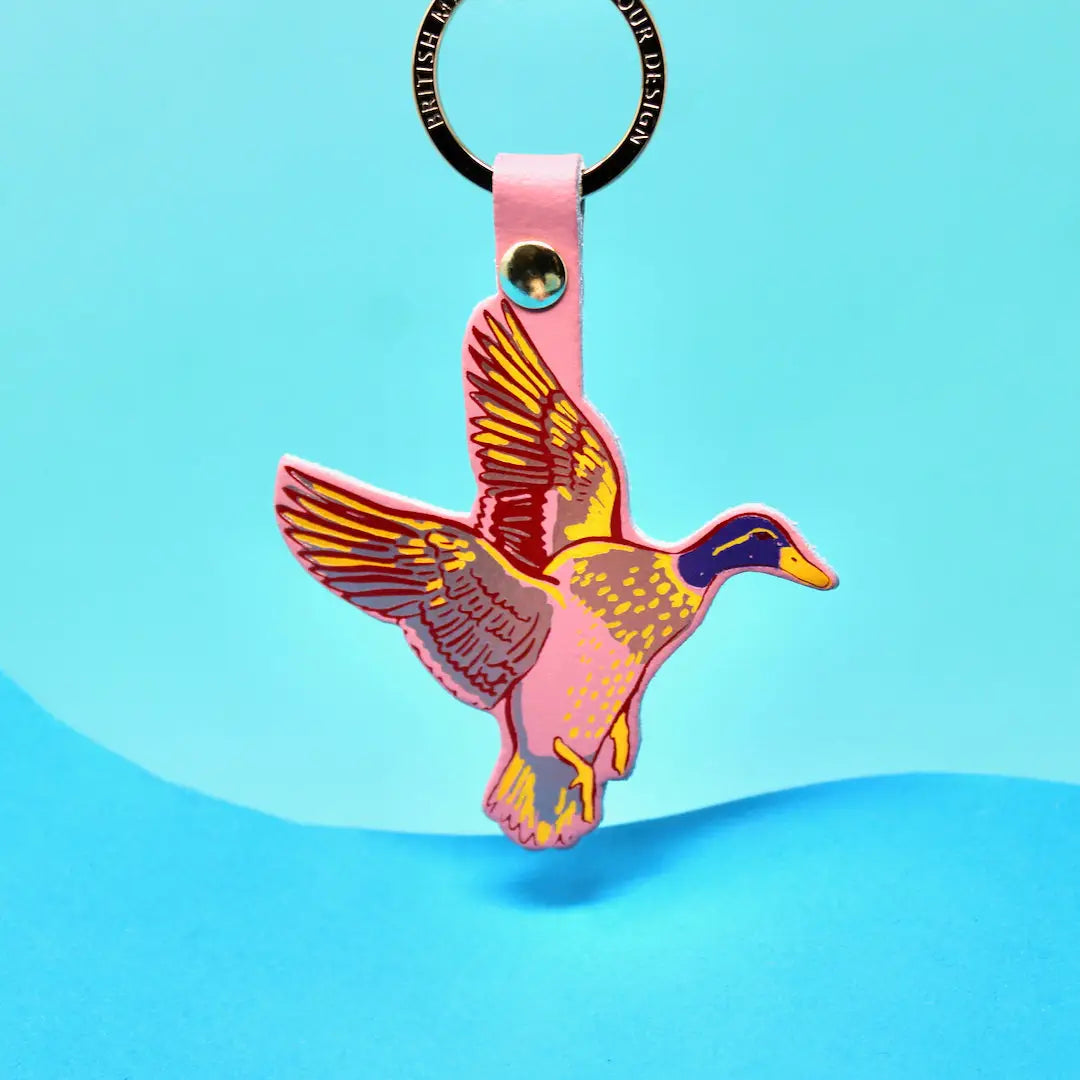 Ark Colour Design flying duck keychain with pink strap, gold ring, and colorful bird illustration on a bright blue background.