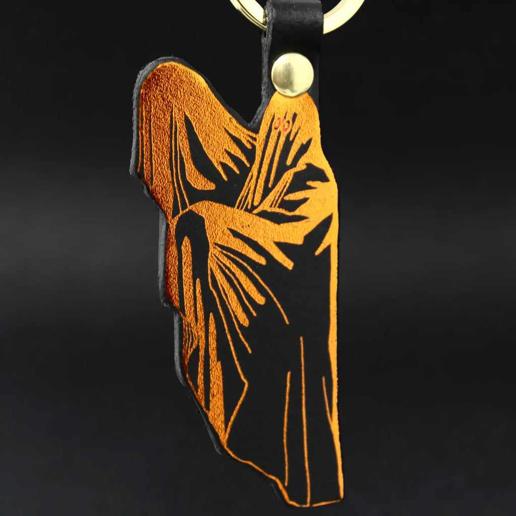Ark Colour Design ghost keychain with black leather strap, gold ring, and orange ghost illustration on a black background.