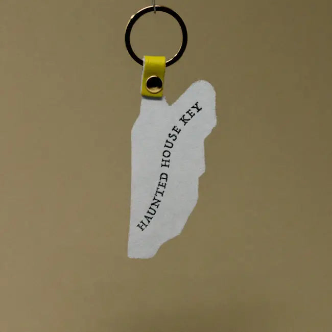 Back side of Ark Colour Design haunted house keychain with “Haunted House Key” text, yellow strap, and gold key ring.