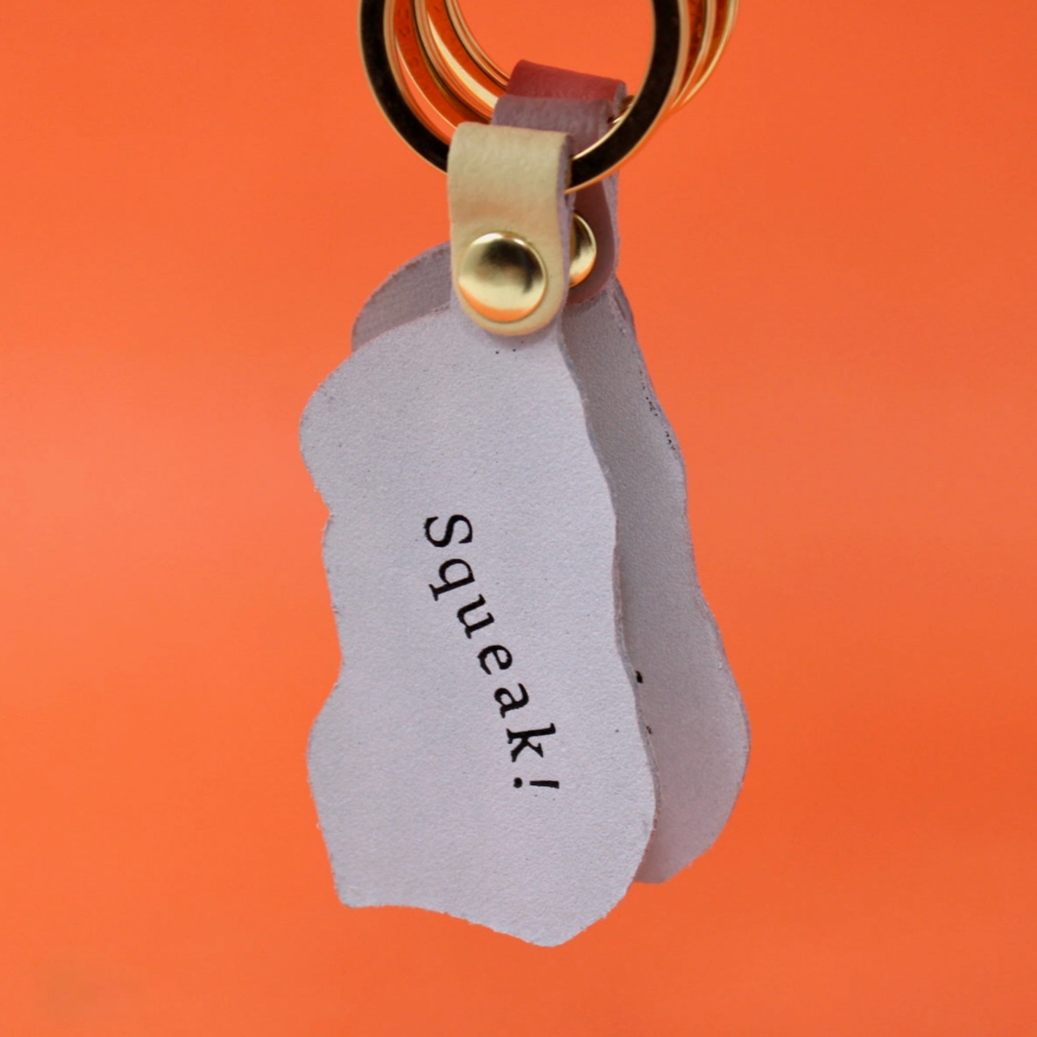 Back side of Ark Colour Design guinea pig keychain with “Squeak!” text, gold key ring, and orange background.