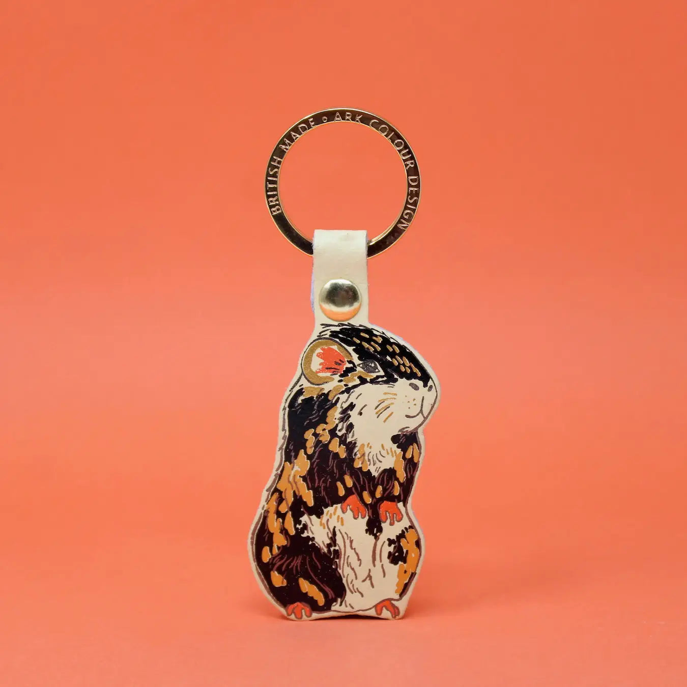 Ark Colour Design guinea pig keychain with a gold ring and illustrated black, cream, and tan guinea pig design.