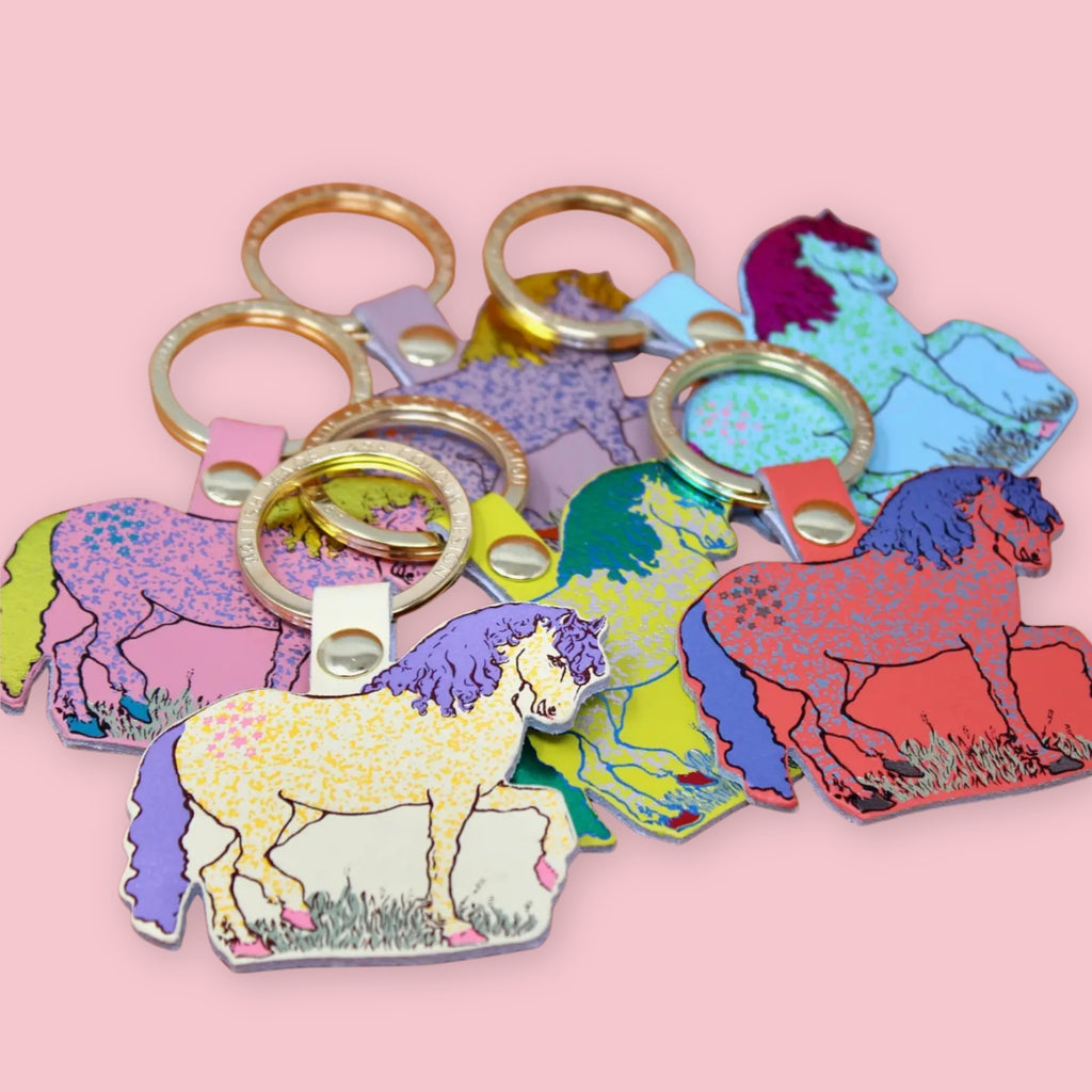Ark Colour Design horse keychains in assorted bright colors, shown with gold key rings on a pink background.