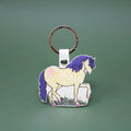 Ark Colour Design horse keychain with gold ring, cream leather loop, and illustrated cream horse design on a green background.