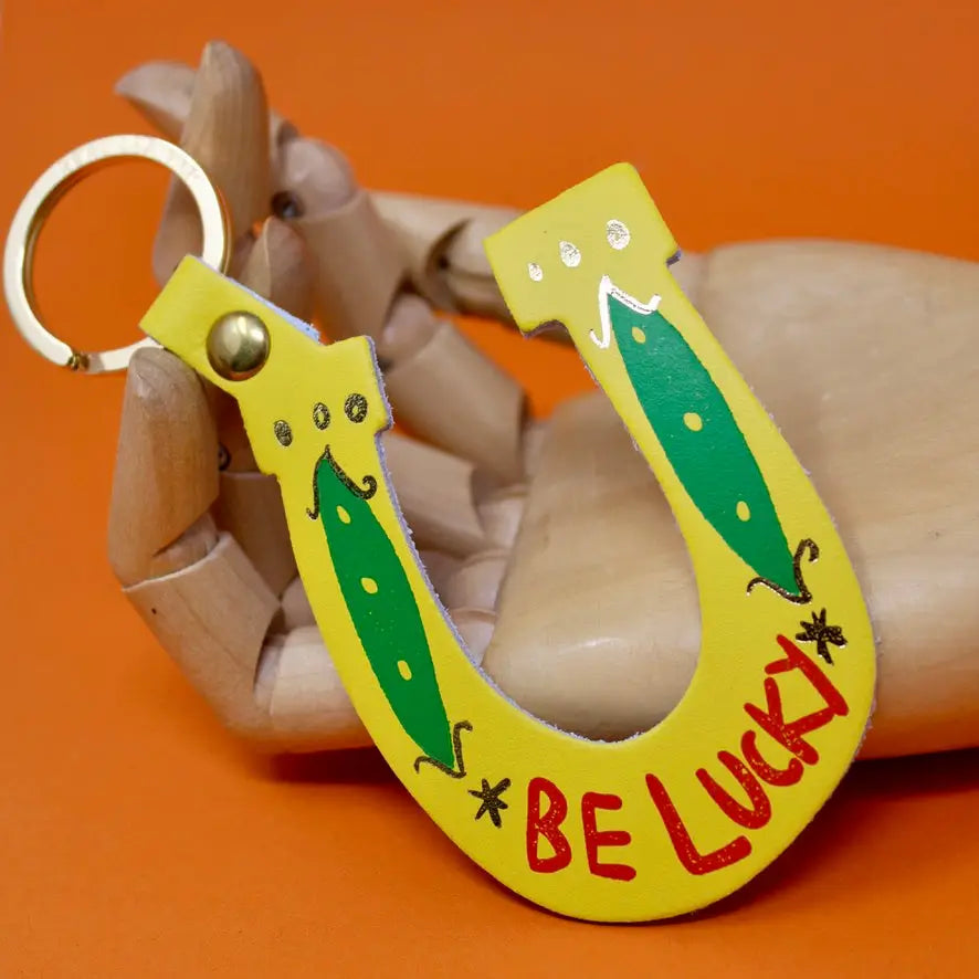 Ark Colour Design yellow horseshoe keychain with green clover design, “Be Lucky” text, and gold key ring.