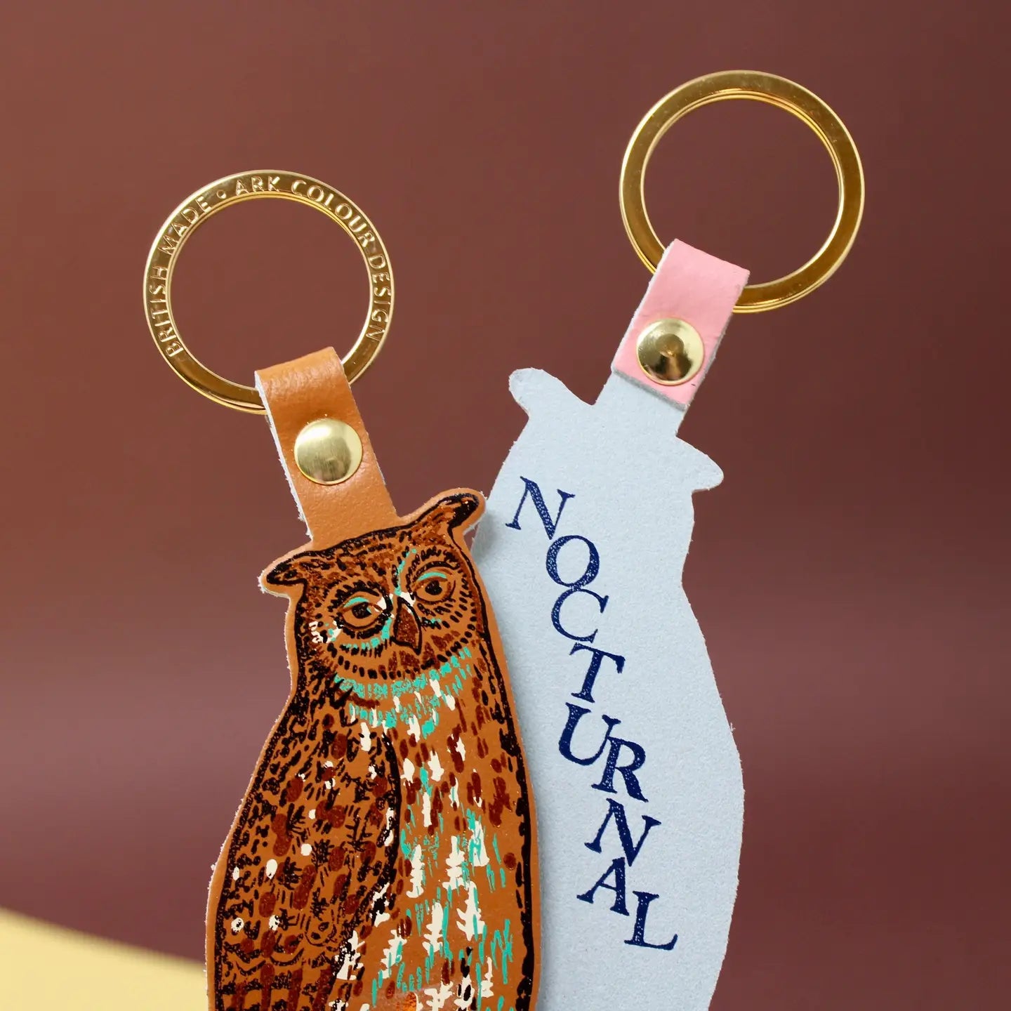 Ark Colour Design owl keychain shown front and back, with gold key rings, leather loops, and “Nocturnal” text on the reverse.