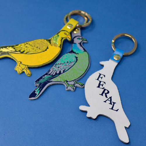 Three bird-shaped keychains on a blue background with one showing its backside with the text reading "FERAL"