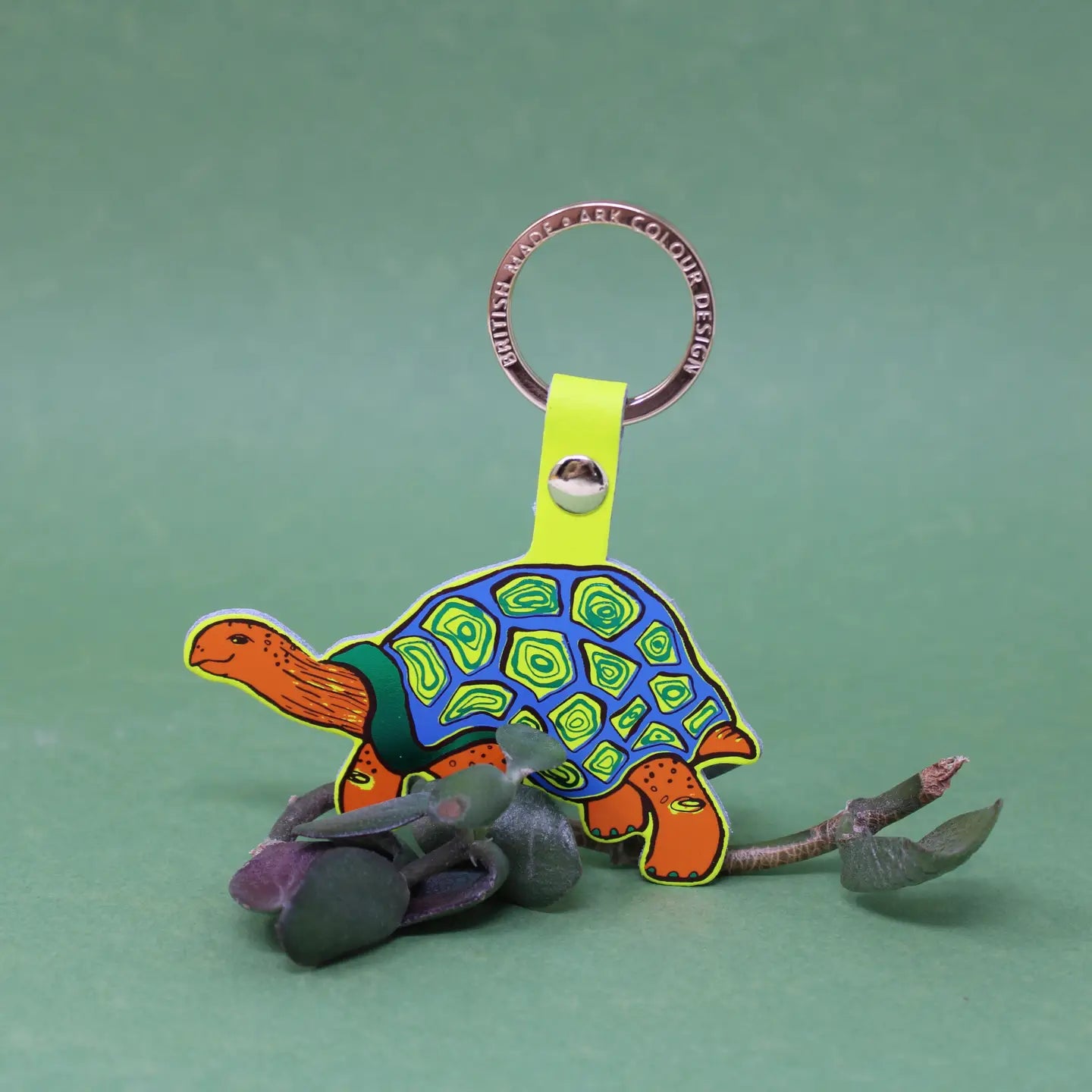 Ark Colour Design tortoise keychain with neon yellow strap, gold ring, and colorful illustrated turtle design.