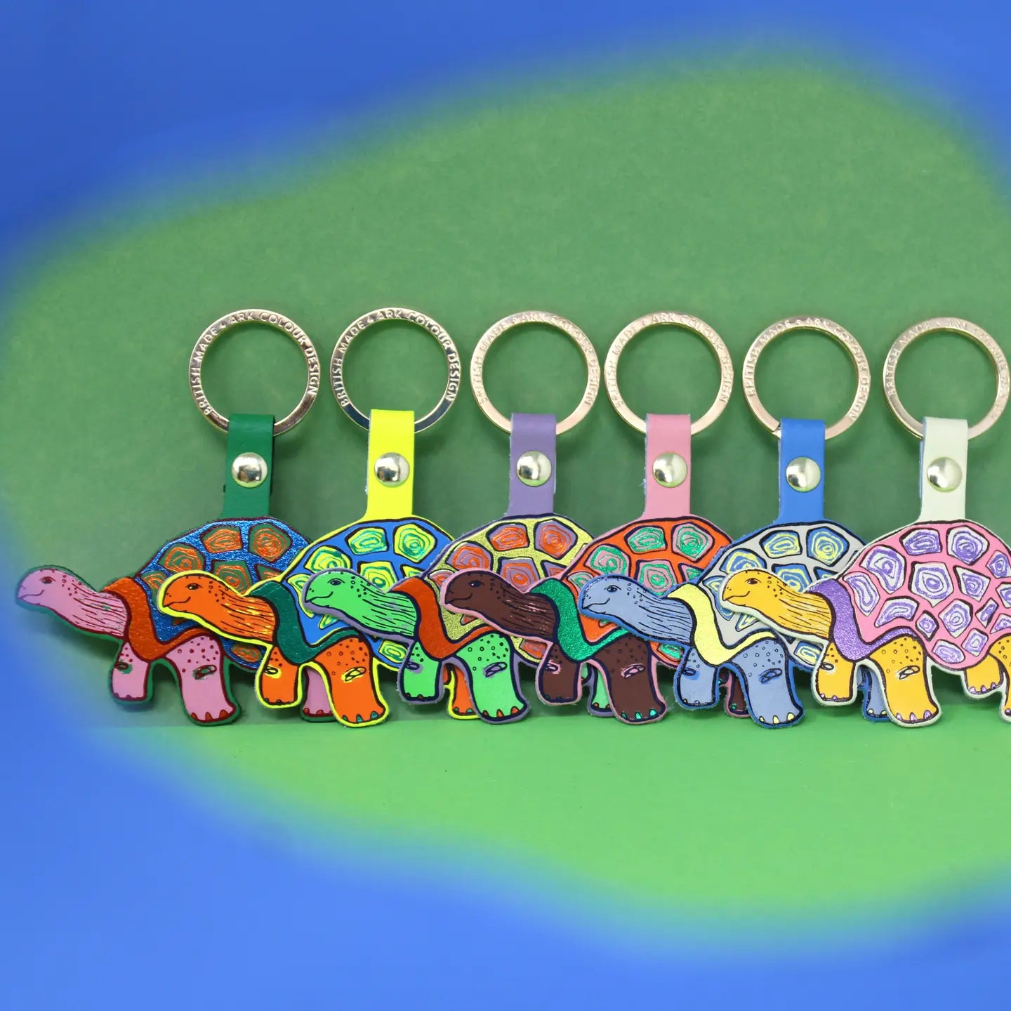 Ark Colour Design tortoise keychains in assorted colors, shown in a row on a green and blue background.