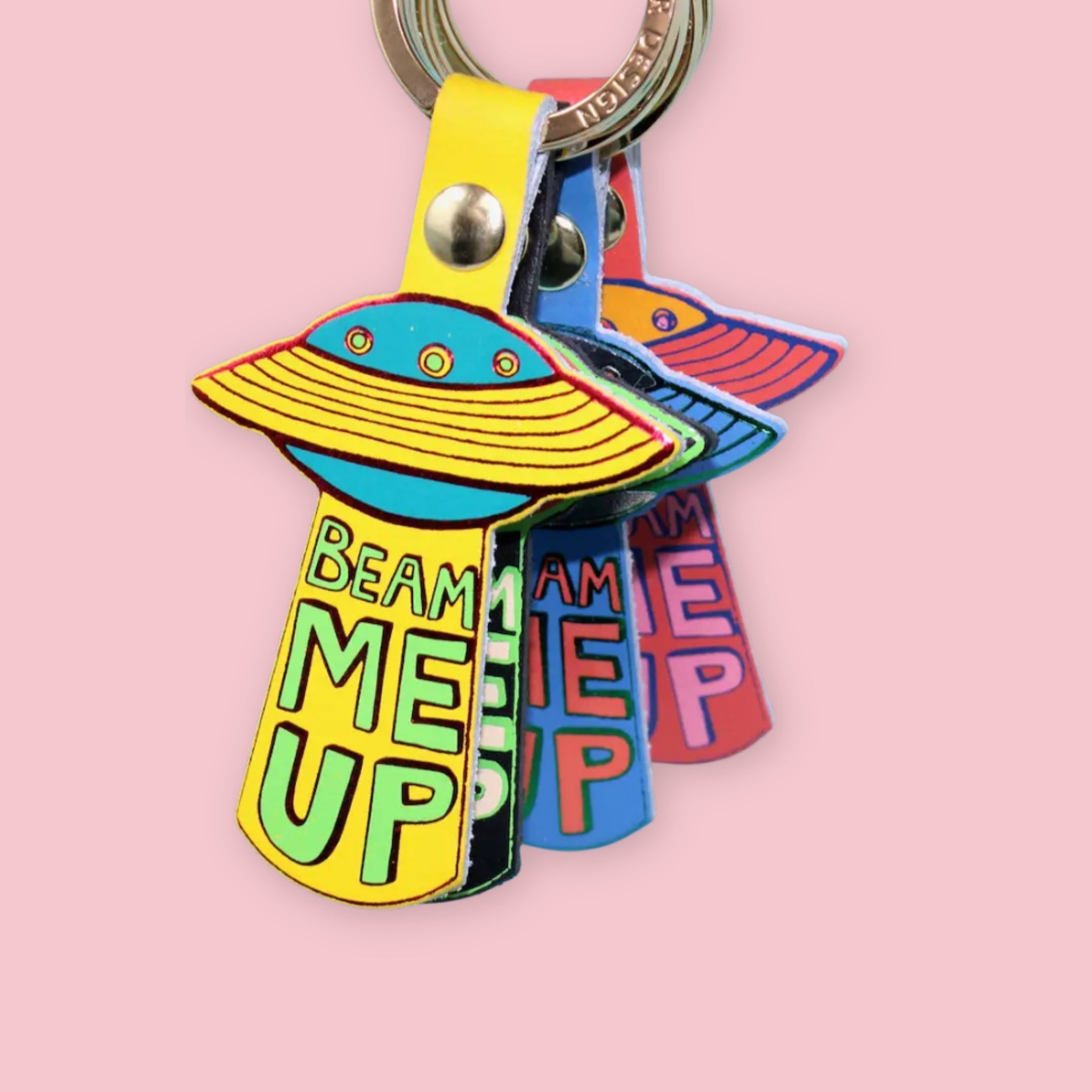 Ark Colour Design UFO keychains in assorted colors with gold rings, shown layered together on a pink background.