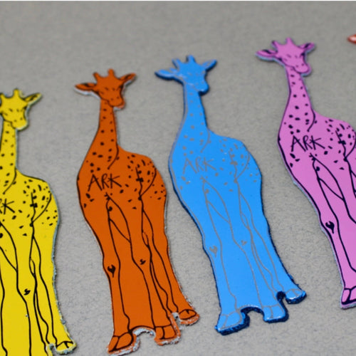 Set of four colorful leather bookmarks shaped like giraffes, arranged in a row on a grey background.
