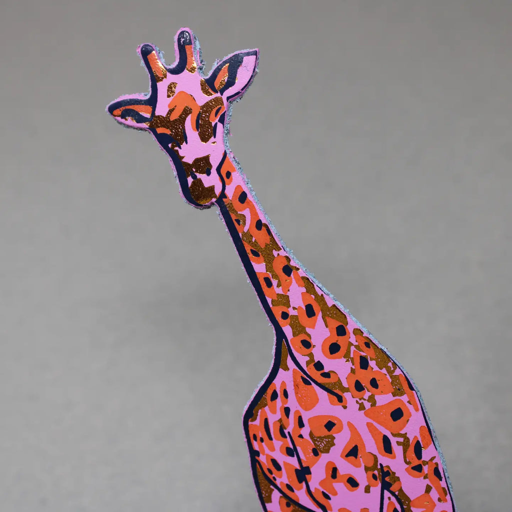 Close-up of a pink and orange giraffe-shaped leather bookmark on a gray background.
