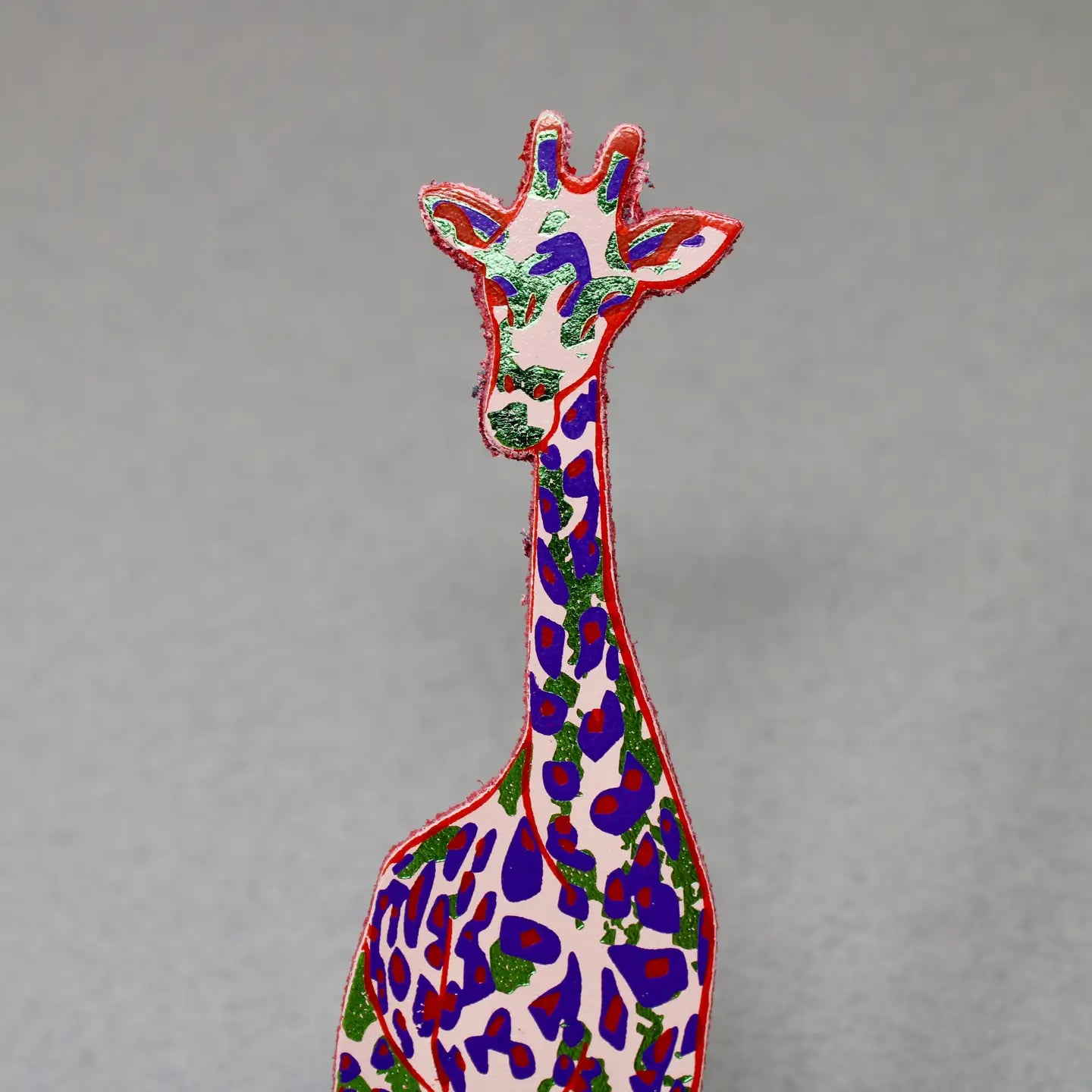 Close-up of a pink and blue giraffe-shaped leather bookmark on a gray background.
