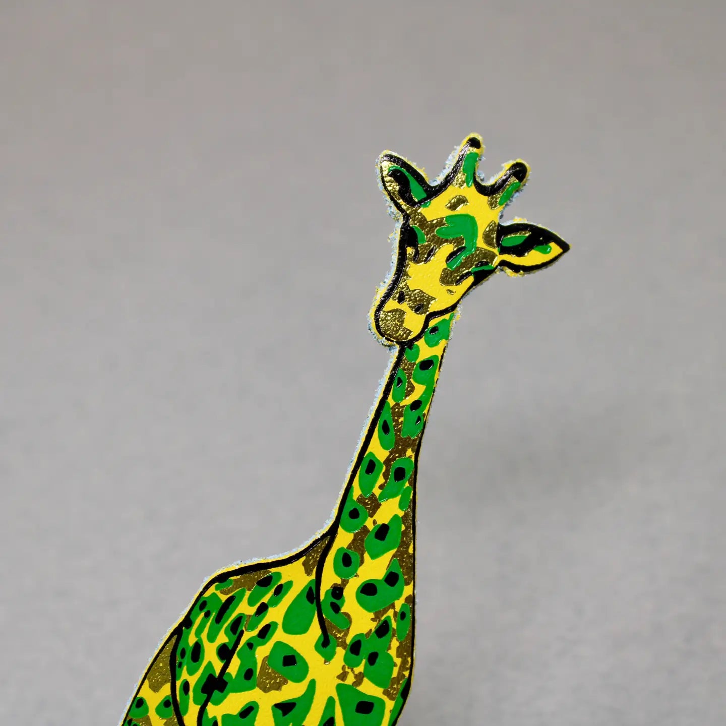 Close-up of a yellow and green giraffe-shaped leather bookmark on a gray background.