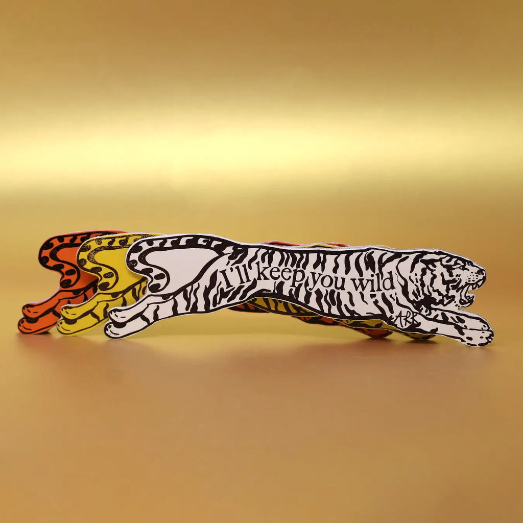 Set of three Ark Colour Design leather bookmarks shaped like leaping tigers with the text 'I'll keep you wild' on the back, shown layered on a gold background.