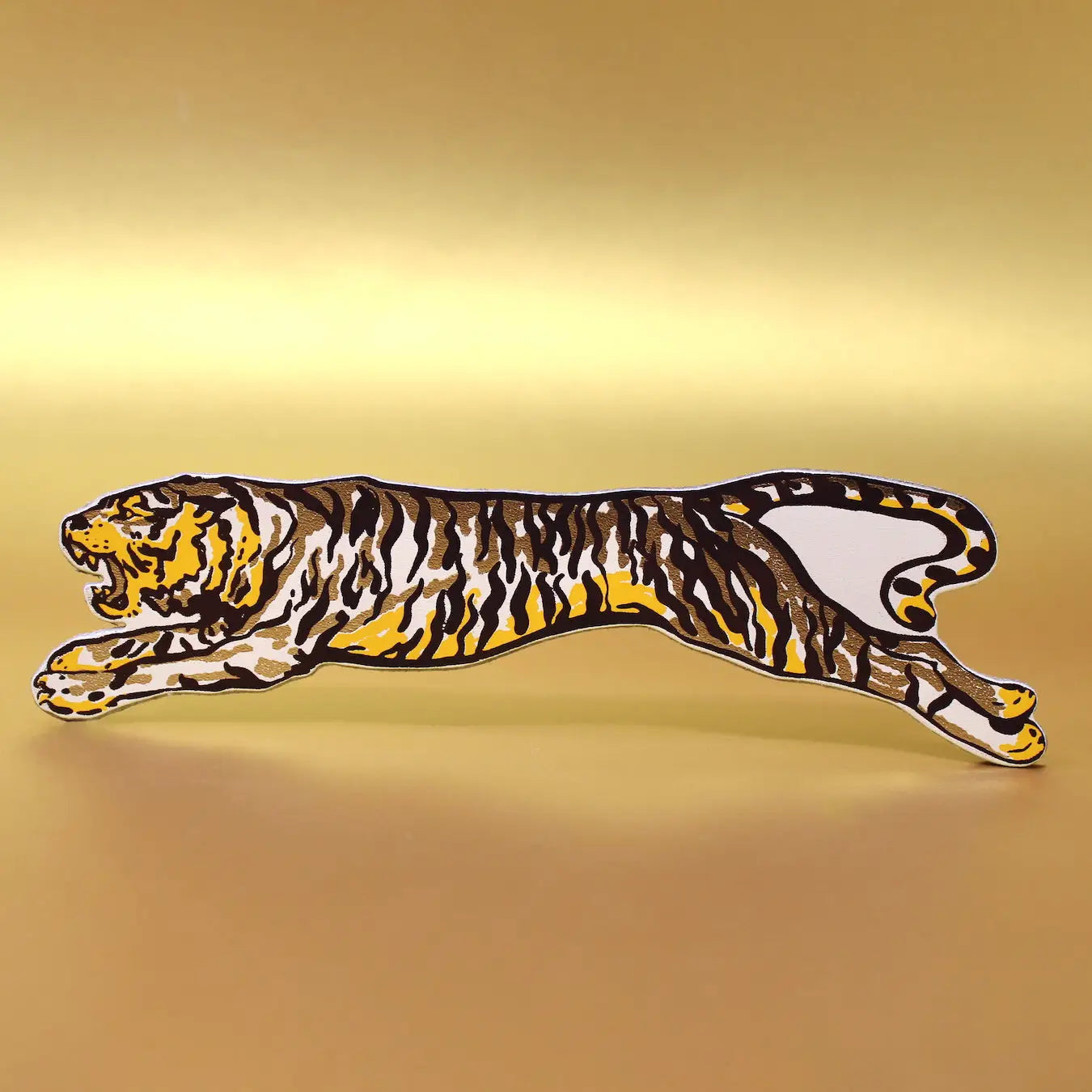 Leaping tiger-shaped leather bookmark with gold, black, and yellow stripes, displayed horizontally on a warm brown background.