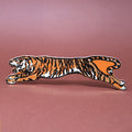 Leaping tiger-shaped leather bookmark with tan, black, and cream stripes, displayed horizontally on a warm brown background.