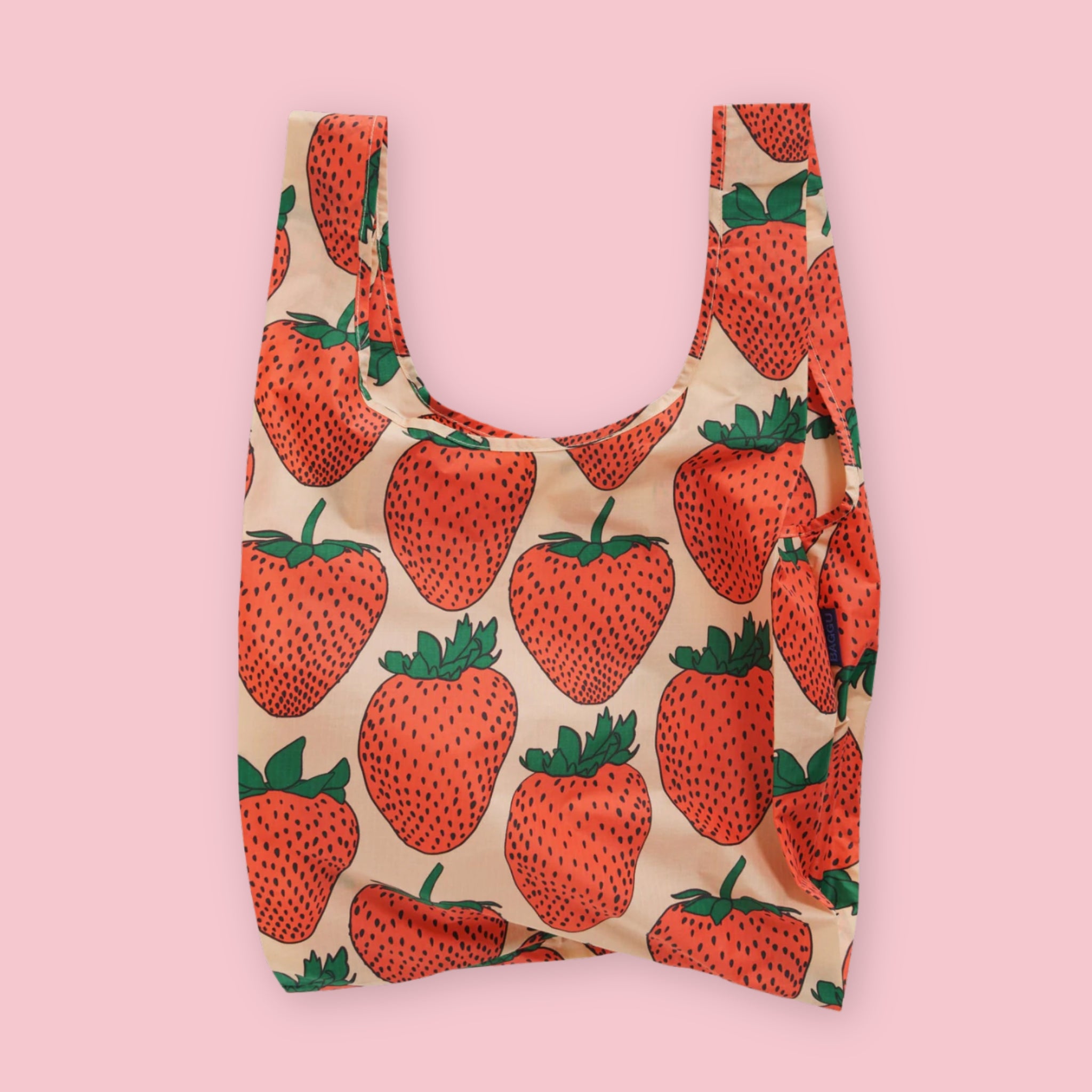 Baggu standard tote in the Strawberry print, featuring large bold strawberry illustrations on a cream background, on a pink background.