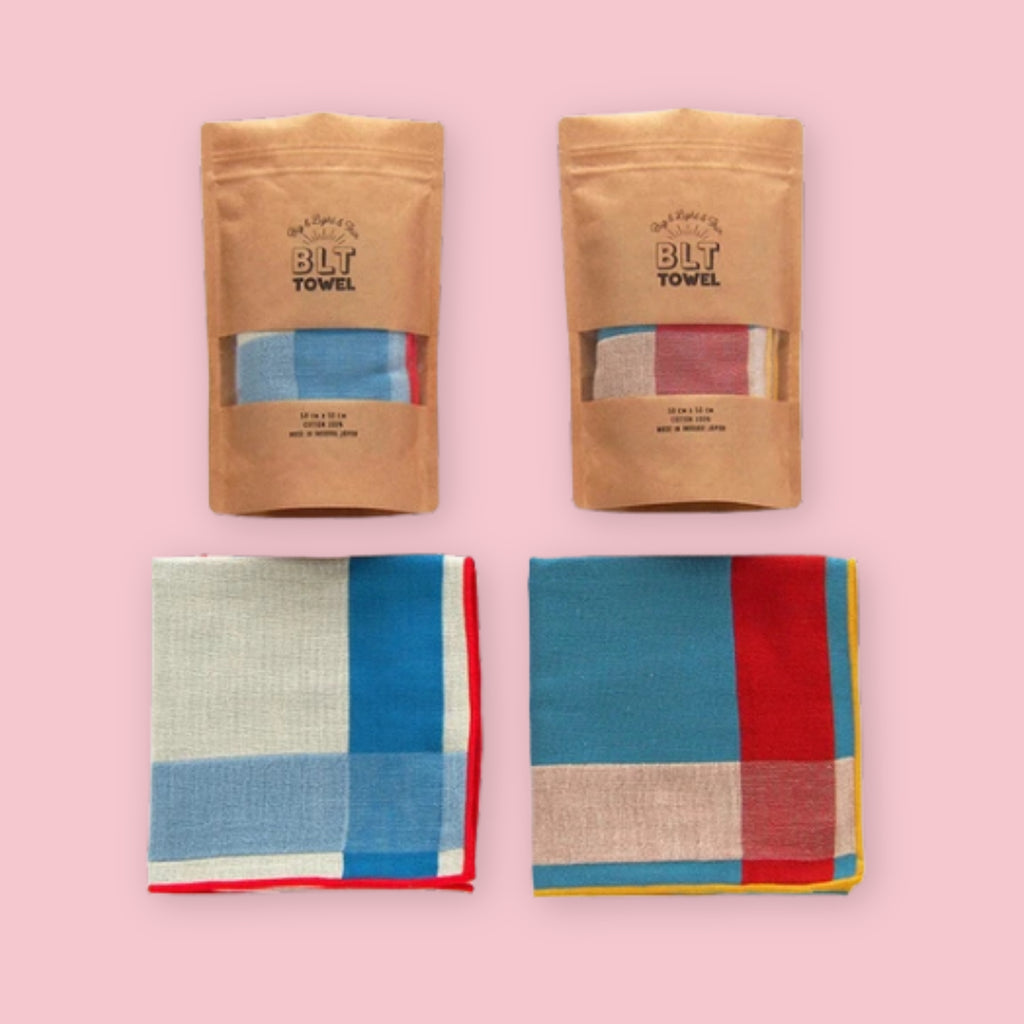Imabari BLT Towel in Bold Blue Stripe and Bold Red Stripe styles, shown folded and in kraft paper packaging on a pink background